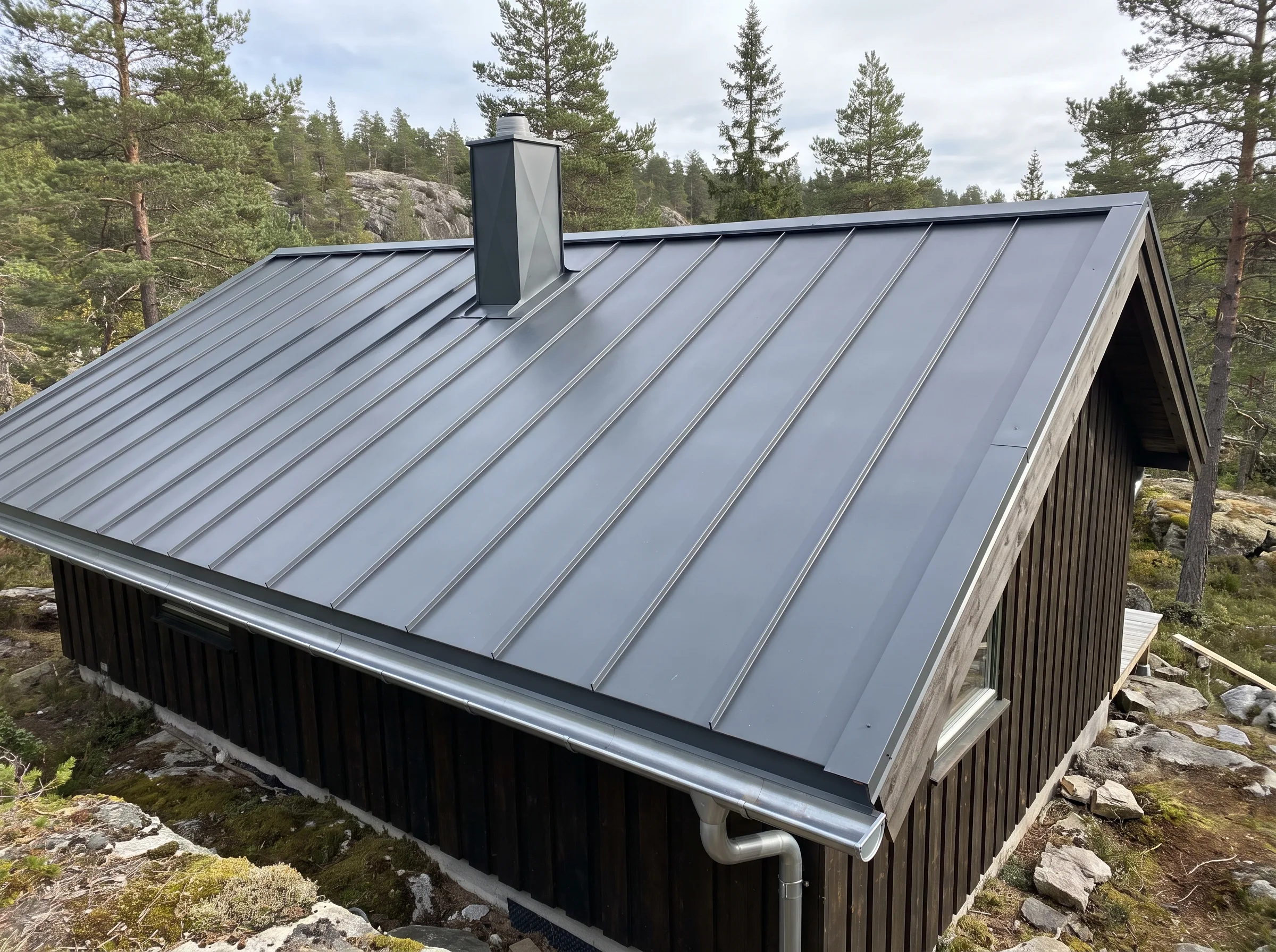Moderne ståltak på hytte med pipe og omgivende skog