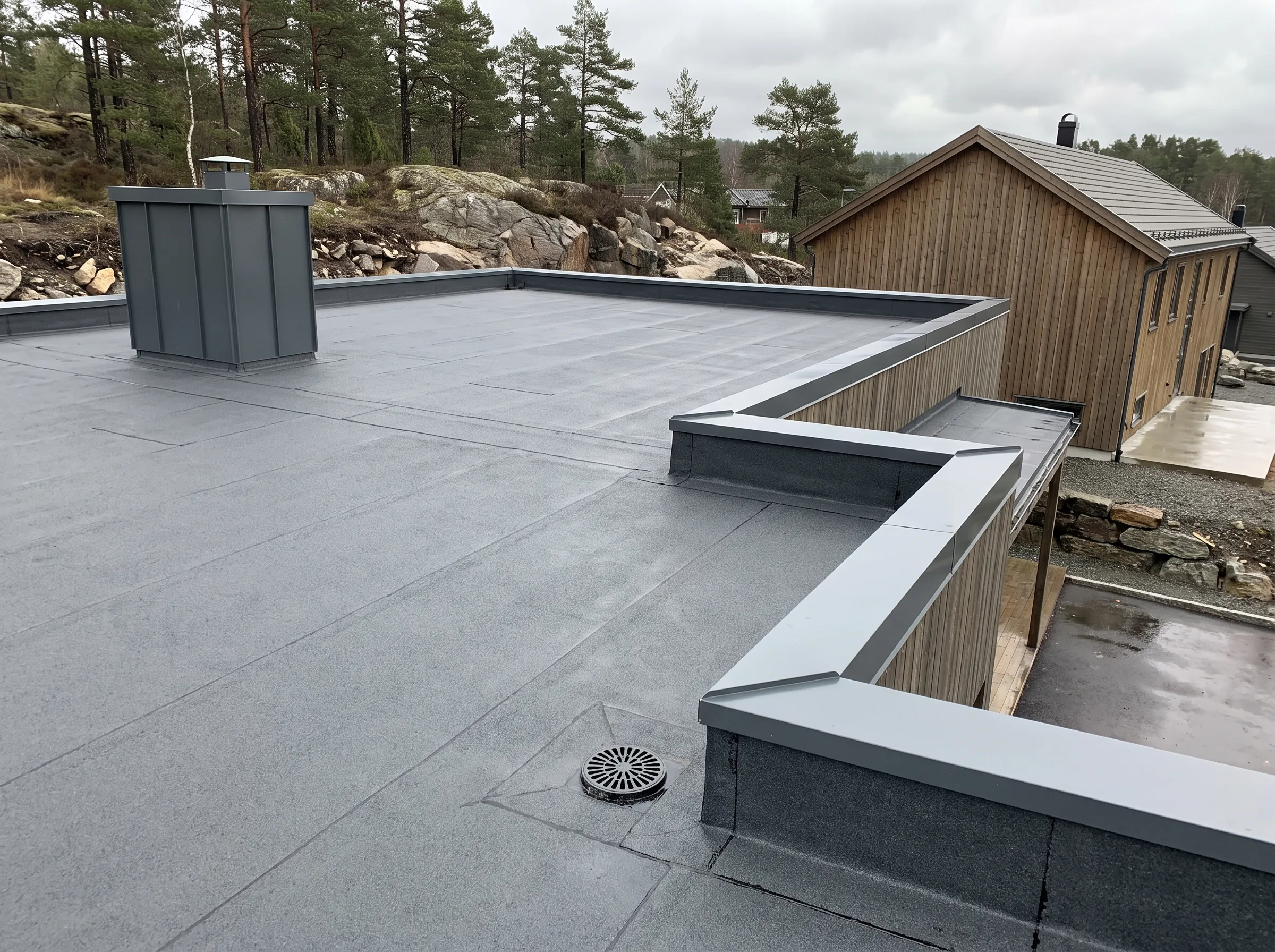 Flatt tak med vanntett belegg og utsikt mot trehus i bakgrunnen
