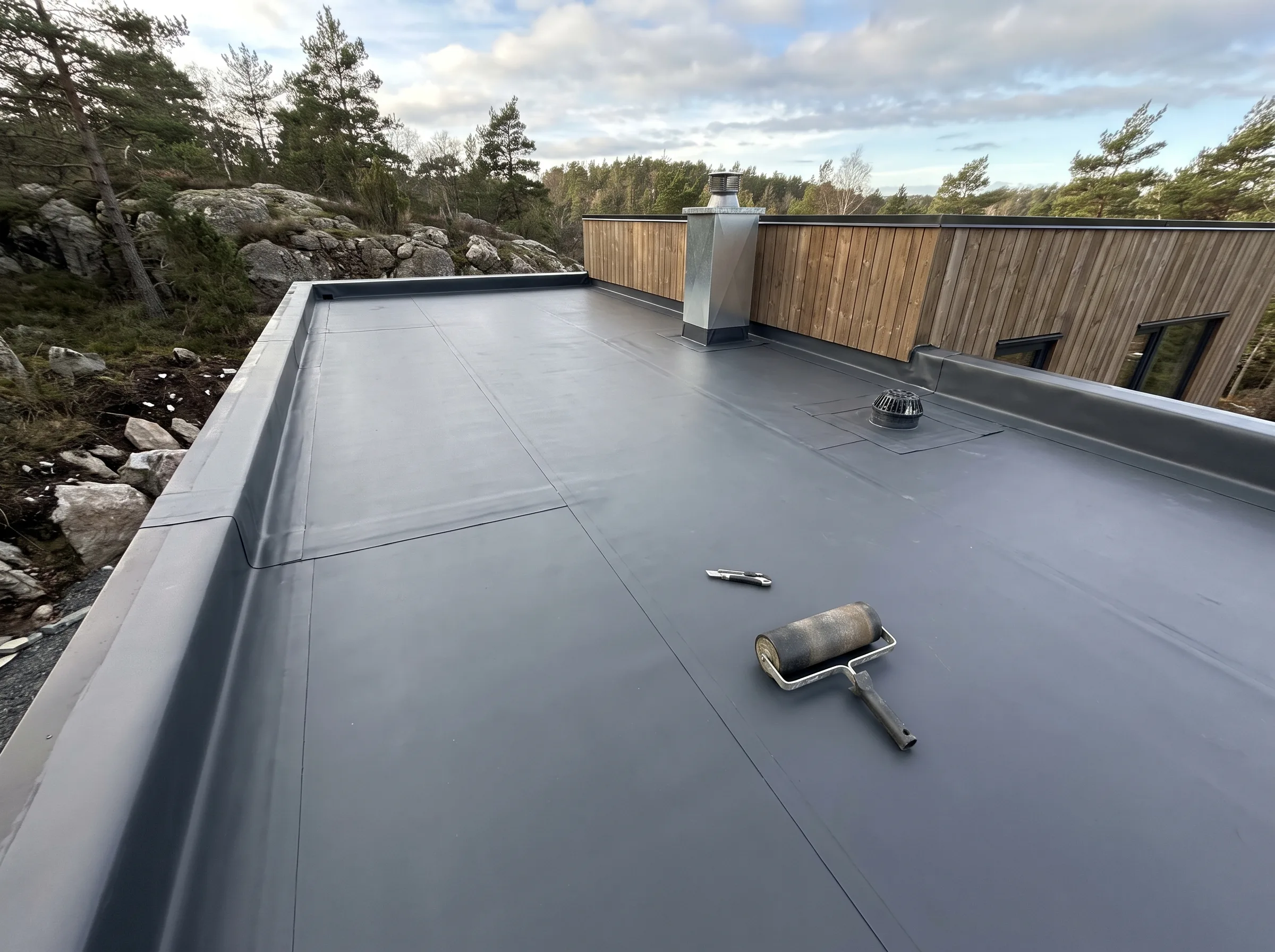 Flatt tak med takmembran, verktøy på takflaten og bygning i bakgrunnen